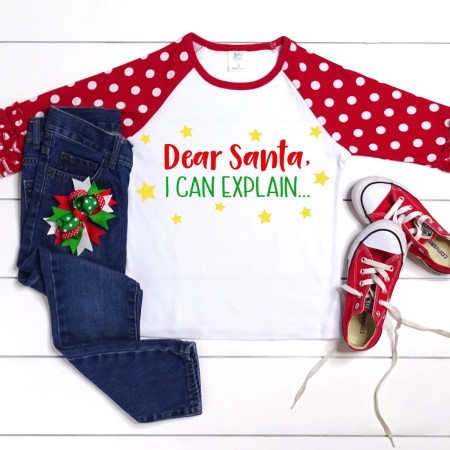 A white shirt with red and white polka dotted sleeves with the saying on the front that says, Dear Santa, I Can Explain