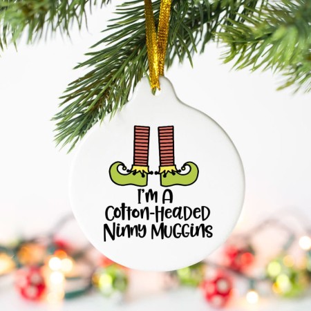 A white Christmas ornament displaying Elf shoes and legs with the saying, I'm a Cotton-Headed Ninny Muggins