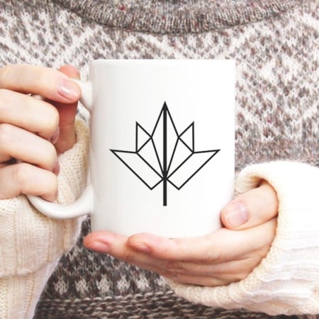 Woman holding a coffee mug decorated with a modern fall leaf
