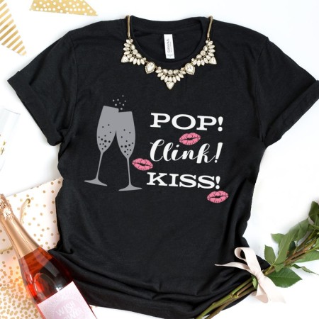 Black t-shirt decorated with champagne glasses and the words Pop! Clink! Kiss!