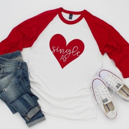 Red and white baseball style shirt with a red hear image that says Single AF