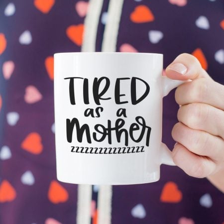 Woman holding a white coffee mug that says Tired as a Mother