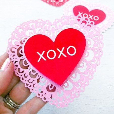 Woman holding a red and pink heart shaped doily that says XOXO