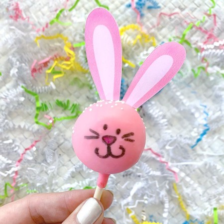 A hand holding a pink Easter bunny cake pop