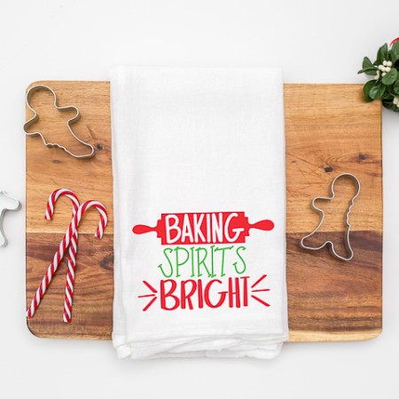 A white kitchen towel decorated with a rolling pin and the saying Baking Spirits Bright