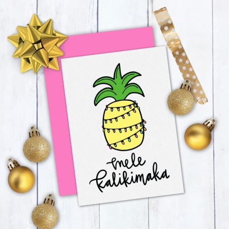 A card decorated with a pineapple with Christmas lights around it and the saying, Mele Kalikimaka