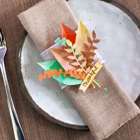 Brown cloth napkin decorated with cutout paper leaves and the word Thankful