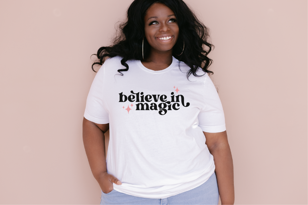 Black model wearing a white t-shirt that says "believe in magic"