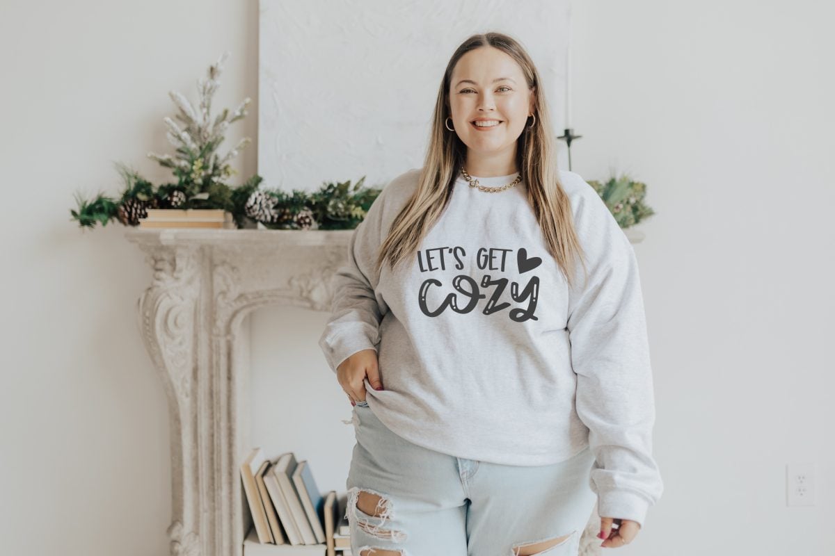 White plus size model wearing a white sweatshirt that says "let's get cozy"