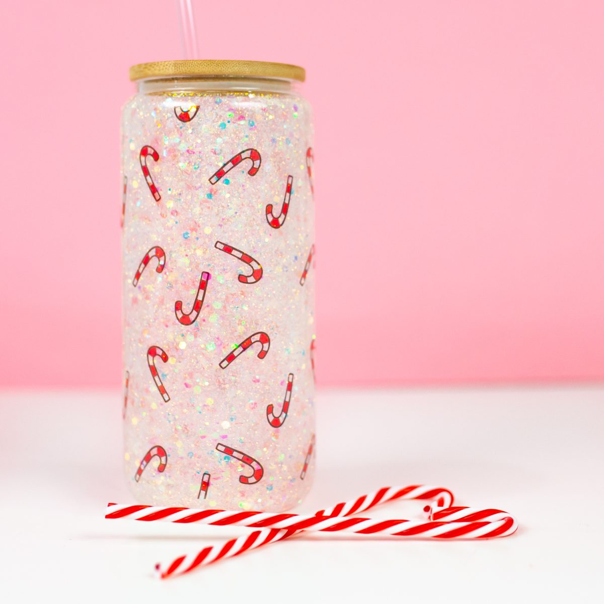 Final candy cane snow globe tumbler with pink background, staged with candy canes