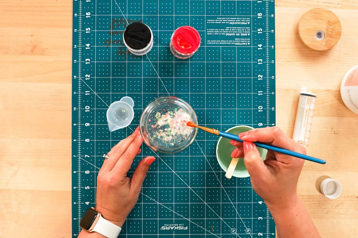 Overhead shot of hands using paint brush to sweep the glitter into the hole in the bottom of the tumbler.