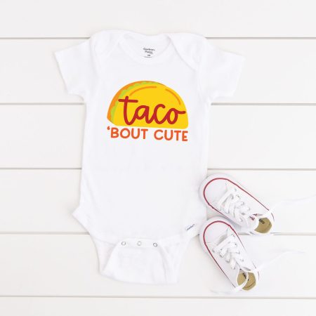 A white onesie with an image of a taco on it and it says Taco 'Bout Cute