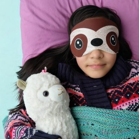 A child wearing a sloth sleep mask and holding a stuffed animal