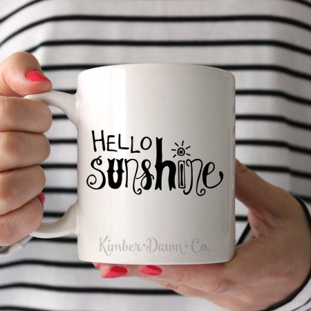 Woman holding a white coffee mug with hand lettered Hello Sunshine SVG design on it