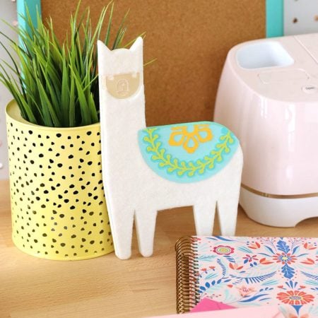 A chipboard llama, potted succulent, Cricut machine and journal sitting on a desk