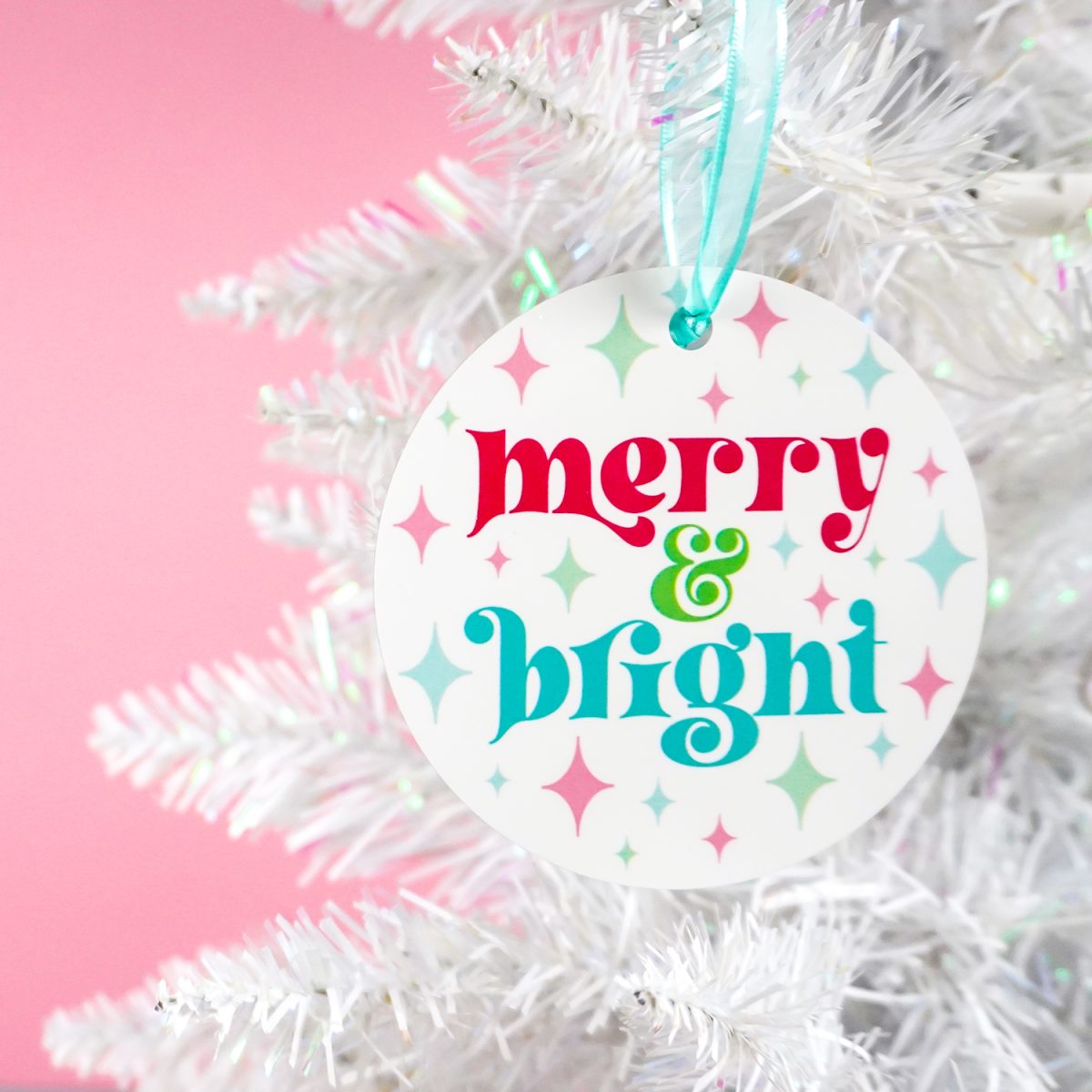 Colorful "merry & bright" ornament on a white Christmas tree with a pink background