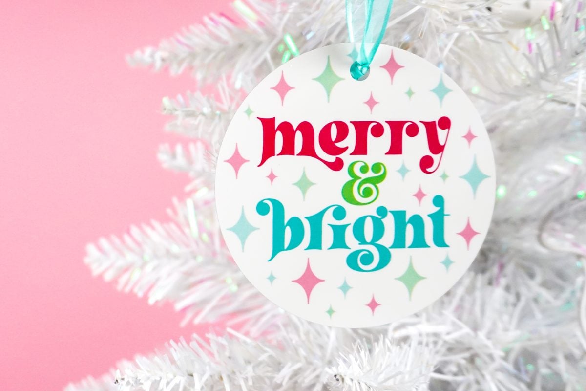 Colorful "merry & bright" ornament on a white Christmas tree with a pink background