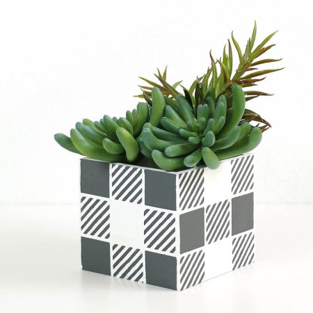 A square buffalo plaid patterned planter with succulents in it