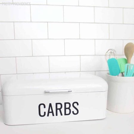 A white bread box sitting on a kitchen counter that says CARBS