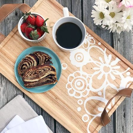 A decorative wood tray with a cup of coffee, toast and bowl of strawberries on it