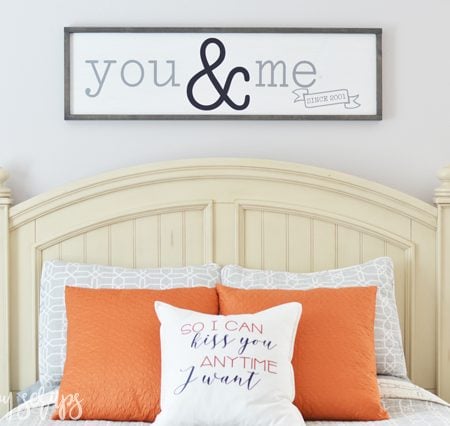 Sign that says You & Me hanging on the wall above a bed