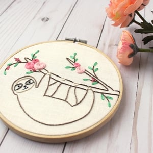 A embroidery hoop with the image of a sloth-embroidered sloth hanging from a tree branch