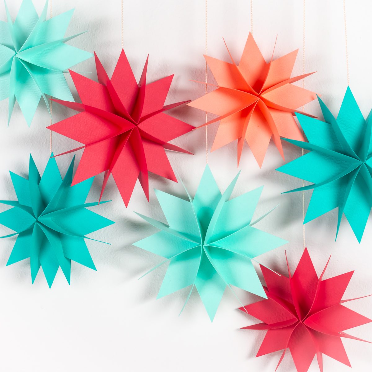 Brightly colored paper Christmas stars hanging over white wall