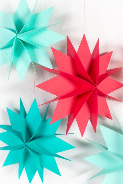 Brightly colored paper Christmas stars hanging over white wall