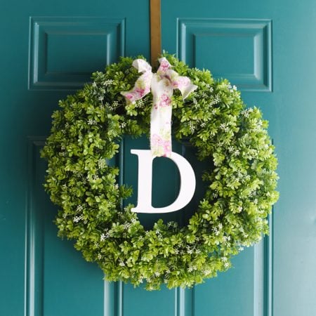Green spring wreath hanging on a door with a monogrammed letter "D" on it