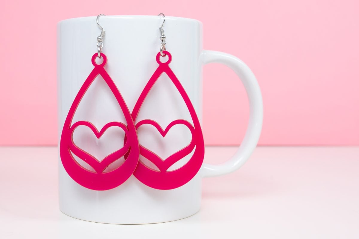 Pink heart earrings hanging on a white coffee cup with a pink background