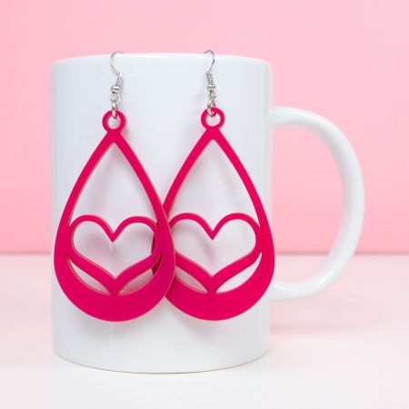 Pink heart earrings hanging on a white coffee cup with a pink background