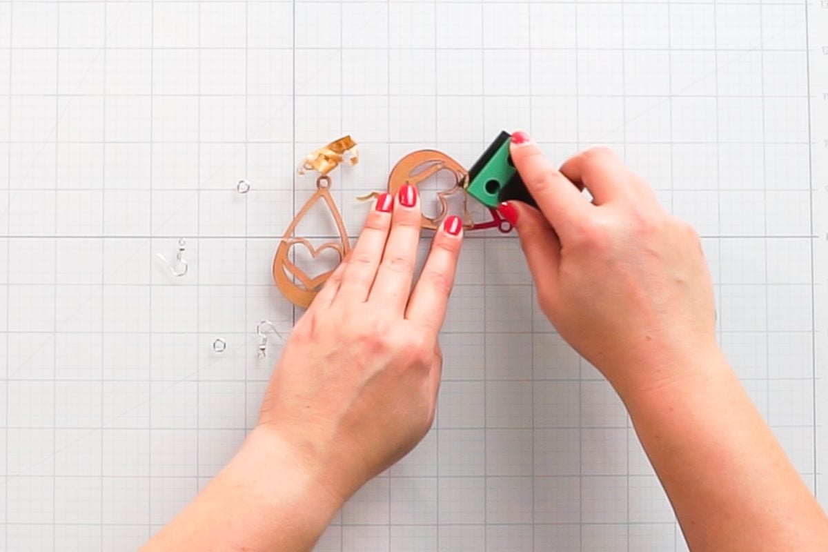 Hands removing masking from earrings using a plastic razor blade.