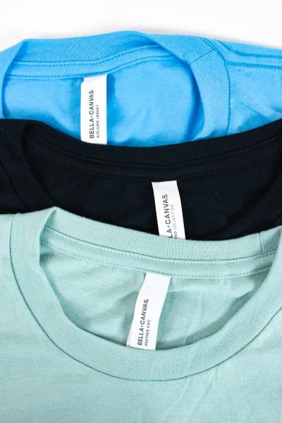 Top down photo of three BELLA+CANVAS shirts blue, black, and mint.