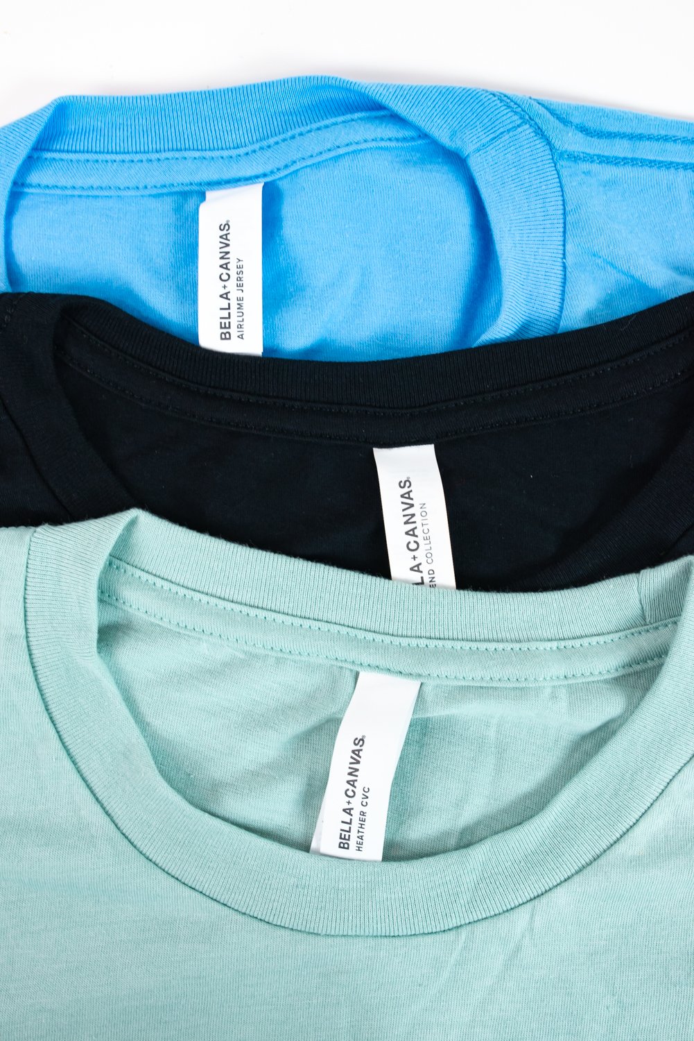 Top down photo of three BELLA+CANVAS shirts blue, black, and mint.