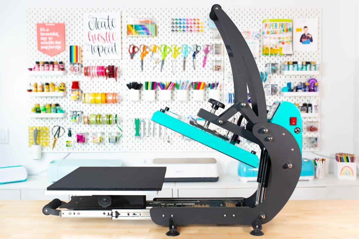 Side view of the teal WALApress sitting on workbench with crafty pegboard behind. Drawer is open.