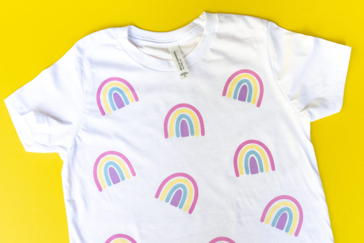 Bella Canvas white shirt with colorful HTV rainbows on it on a yellow background