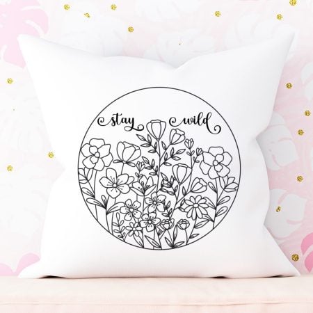 White pillow with a circular wildglower design on it that says, Stay Wild
