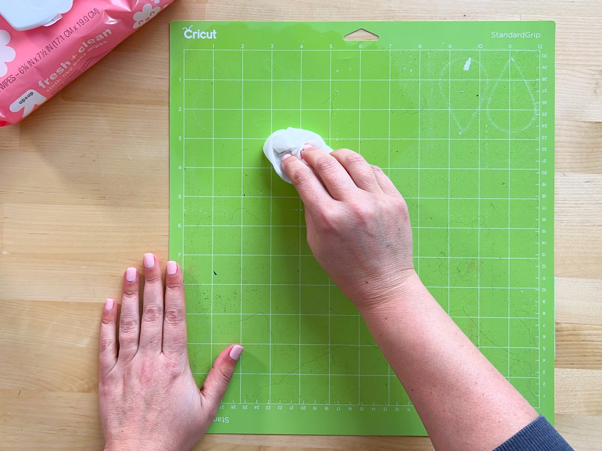 Overhead shot of hands using a baby wipe to clean a Green cricut mat.