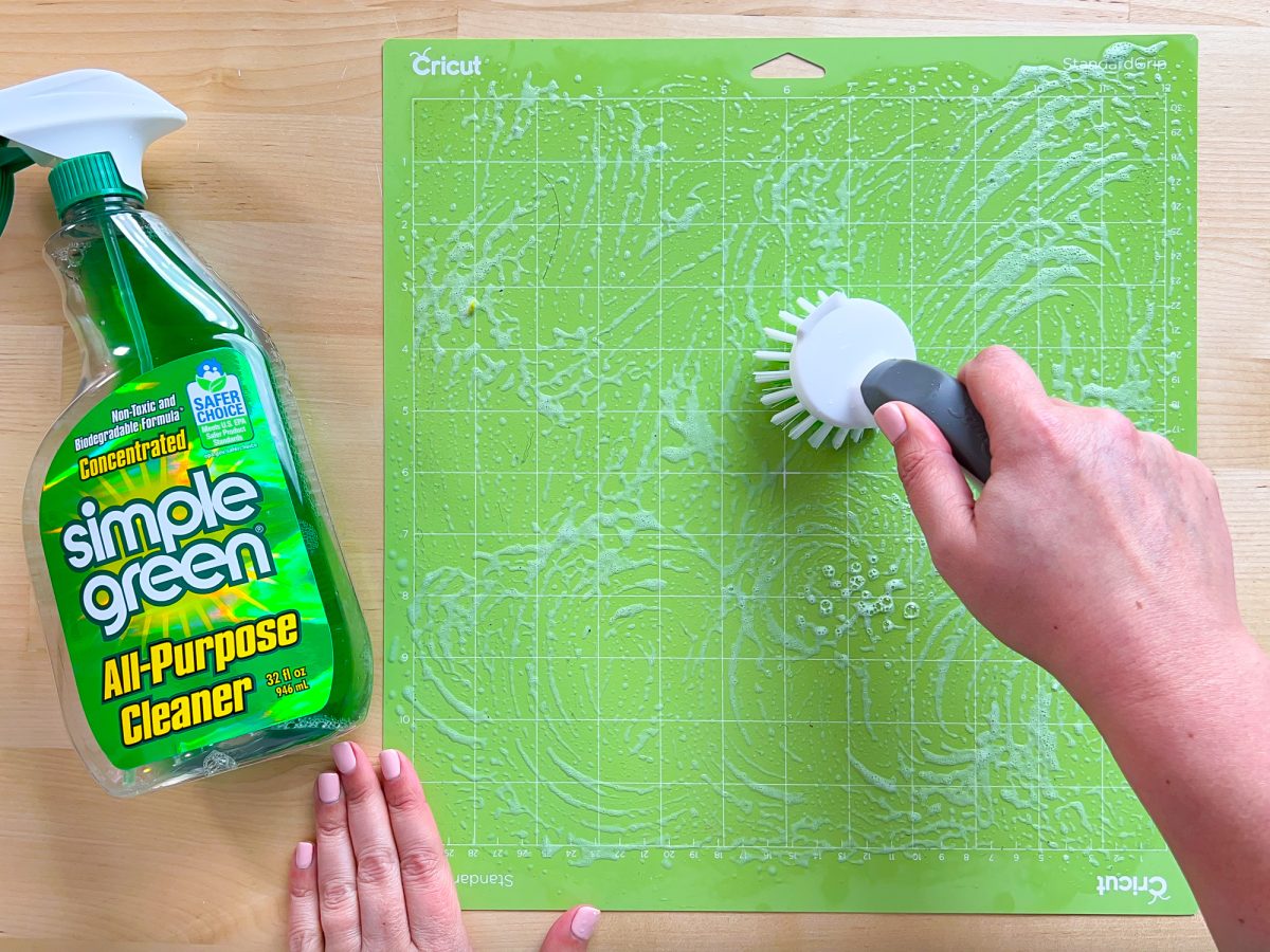 Overhead shot of hands using a bristled brush and Simple Green to clean a Green cricut mat.