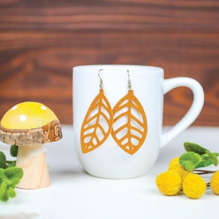 A mushroom figurine next to yellow floral sprig and a coffee mug that has a pair of earrings hanging from it
