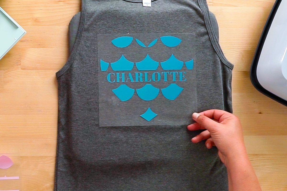 Hands placing the teal layer of HTV on the tank top.