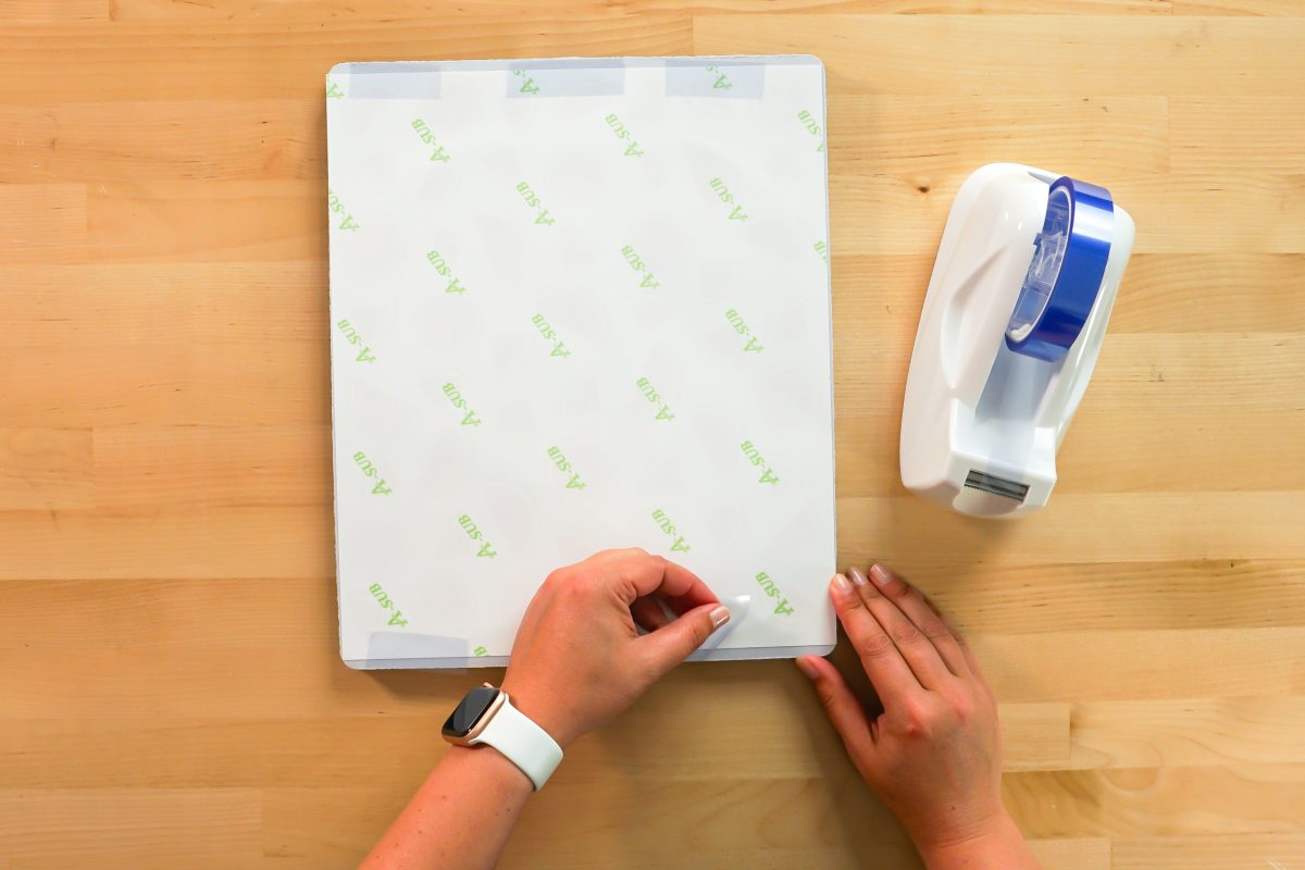 Hands using tape to secure image on blank flip flops