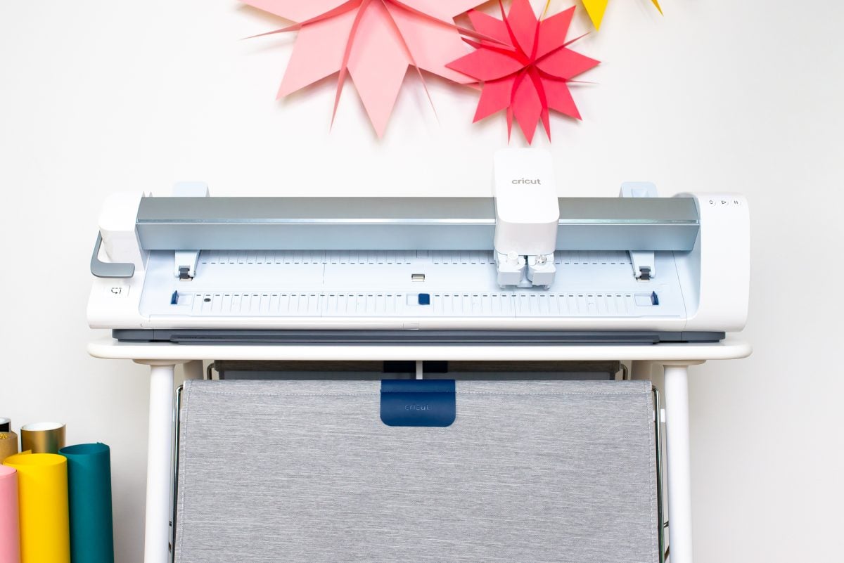Cricut Venture on Cricut Venture Docking Stand with colorful paper stars and rolls of material in a cart next to it.