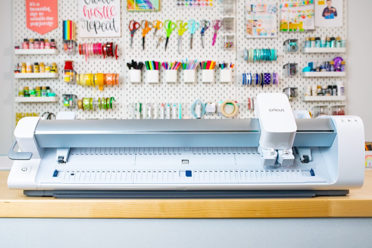 Cricut Venture on a table with a pegboard and colorful supplies behind it.