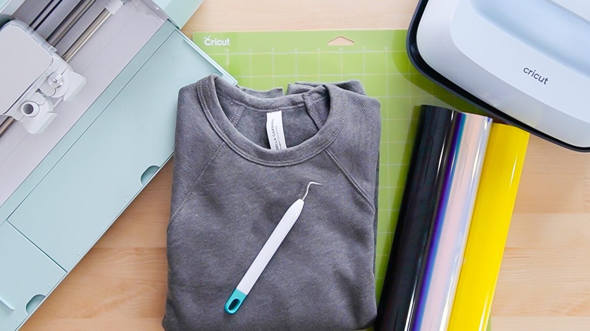 Cricut machine, gray BELLA+CANVAS sweatshirt, and HTV materials for project