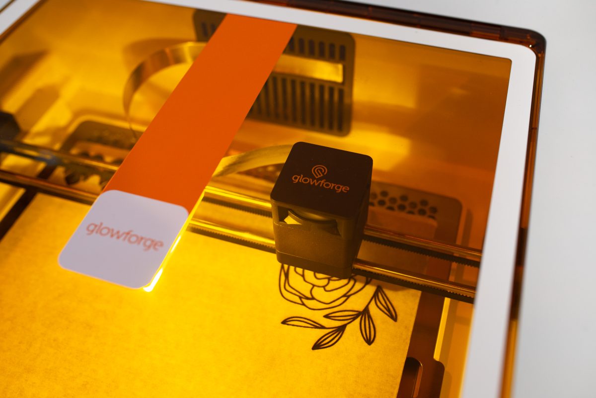 Glowforge Aura cutting a flower design through the orange Aura cover