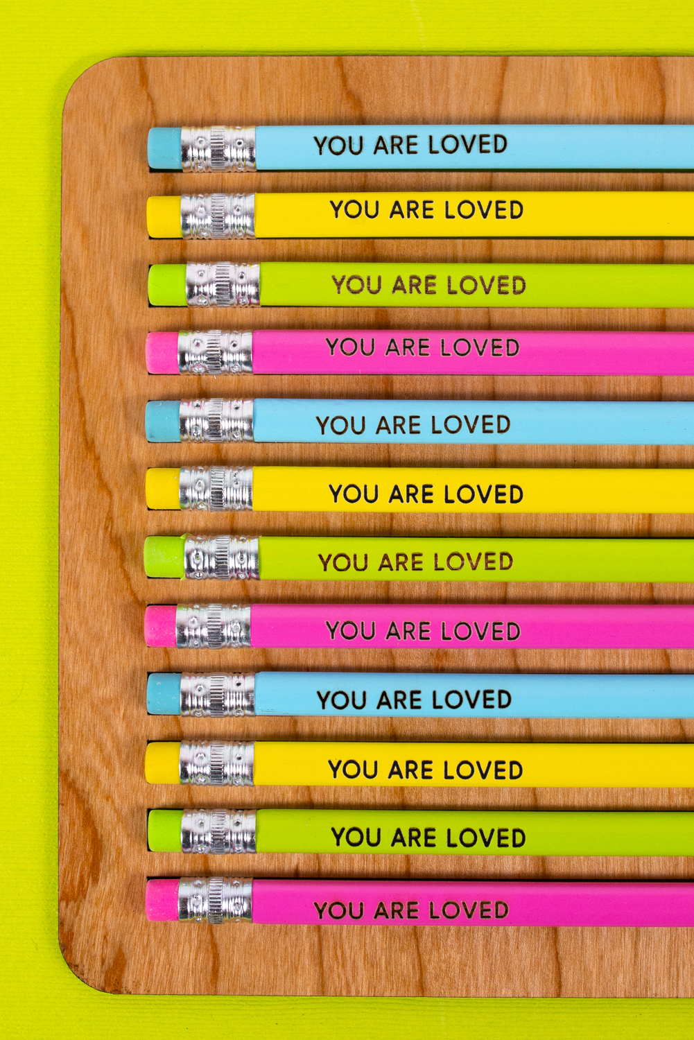 Finished YOU ARE LOVED engraved pencils in pencil jig on green background