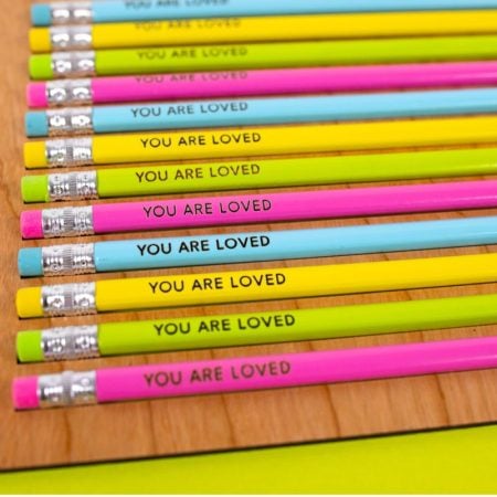 Finished YOU ARE LOVED engraved pencils in pencil jig on green background