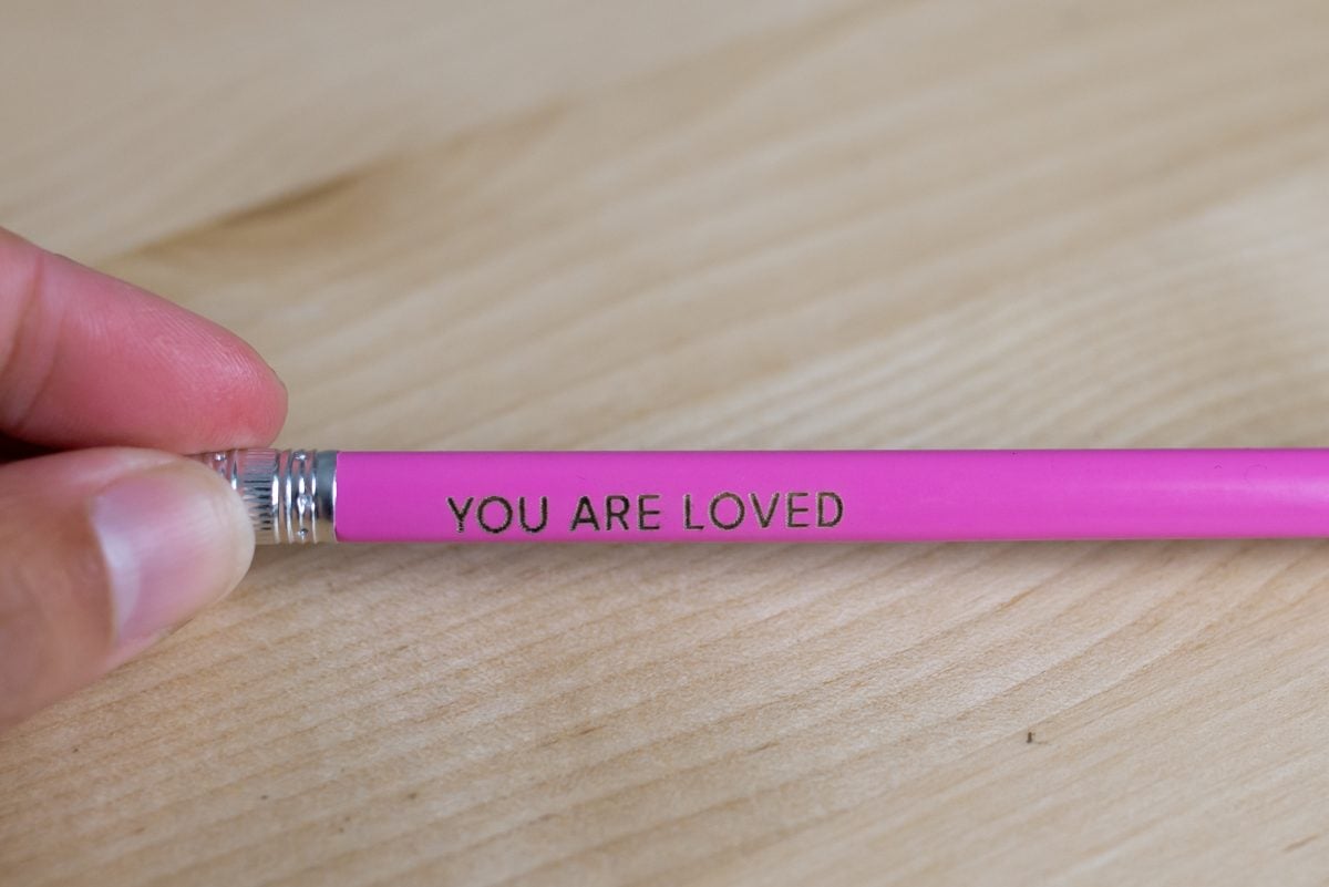 Closeup of pink pencil with YOU ARE LOVED engraving too low