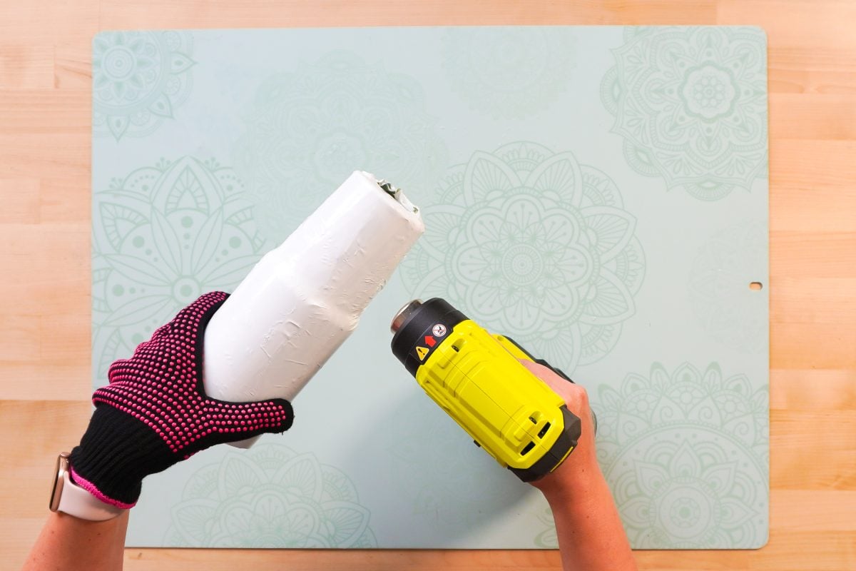 Hands showing how to use a heat gun to shrink the shrink wrap.